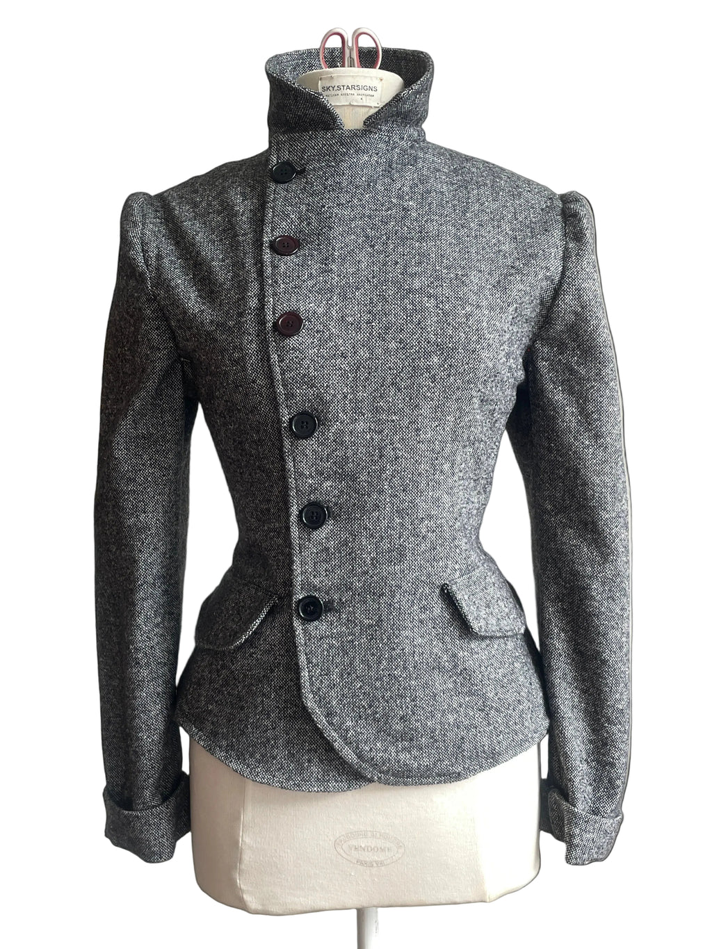 A gray textured wool-blend jacket with a high mock neck and dark buttons, displayed on a cream dress form mannequin.